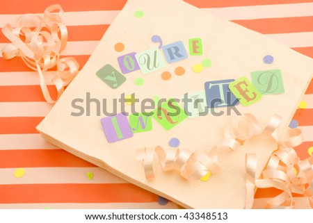 cut out letters spelling you\'re invited on beige napkins with curled ribbons and confetti, great for invitation cards on an orange striped background