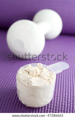 A scoop of vanilla powder protein with dumbell in the background on a purple exercise mat.