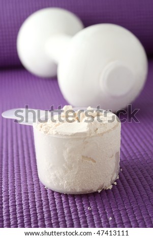 A scoop of vanilla powder protein with dumbell in the background on a purple exercise mat. (shallow depth of field)