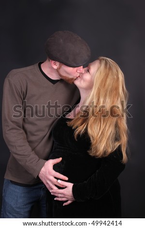 Loving kissing  couple expecting baby, both are touching woman\'s pregnant belly on a black background