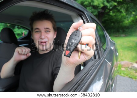 Teenage boy showing excitement holding a modern car key while sitting behind the wheel. Conceptual for new car purchase, or new driver\'s lisence