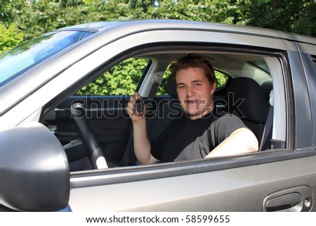 Teenage boy showing while holding a modern car key sitting behind the wheel. Conceptual for new car purchase, or new driver\'s lisence
