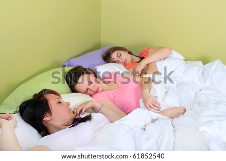 Three pretty teenage girls sleeping on a bed at a sleepover or a slumber party