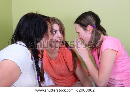 Three teenage girls have a slumber party or sleepover and one is whispering secrets in the other\'s ear