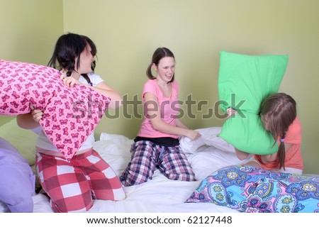 Three teenage girls in their pajamas with pigtails or braids having a pillow fight on a bed at a sleepover