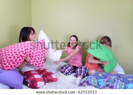 Three teenage girls in their pajamas with pigtails or braids having a pillow fight on a bed at a sleepover