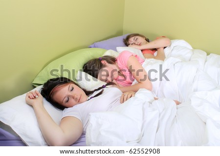 Three pretty teenage girls sleeping on a bed at a sleepover or a slumber party