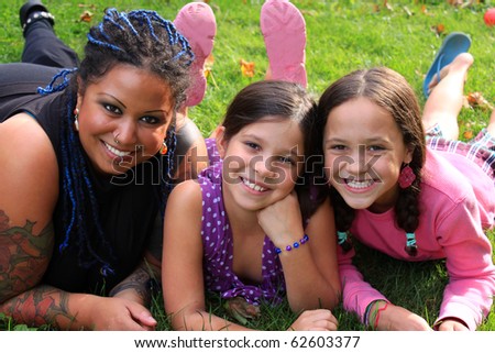 Funky pierced mother laying on the grass with her adolescent daughters smiling happily