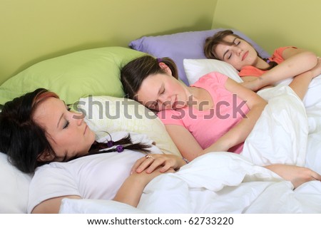 stock photo Three pretty teenage girls sleeping on a bed at a sleepover or