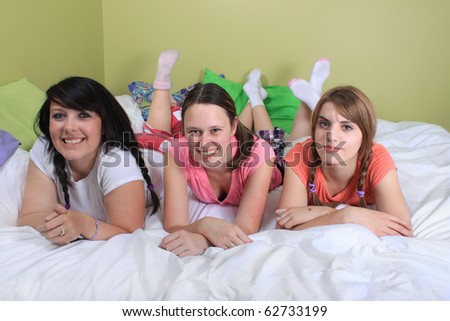 Group of three teenage girls hanging out on a bed in their pajamas ready for a sleepover or slumber party