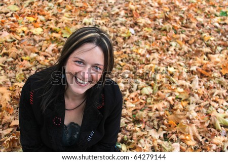 Beautiful woman in her forties is happily sitting on the ground covered by a bed of autumn leaves