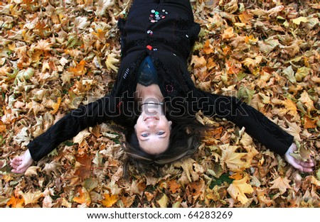 Beautiful woman in her forties is happily laying on the ground covered by a bed of autumn leaves