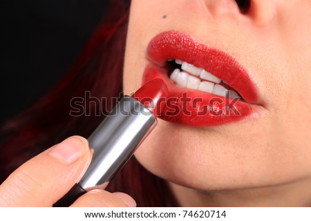 Close-up of woman applying red lipstick to her luscious lips