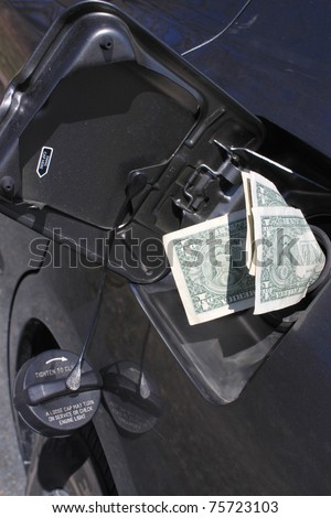 Money sticking out of car's gasoline tank showing the rising cost of fuel