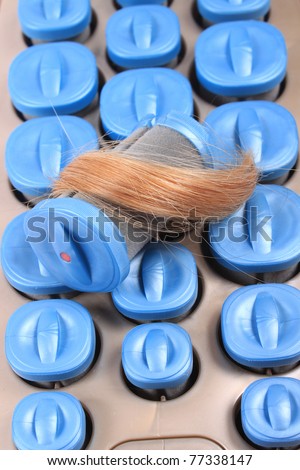 Hot rollers in different sizes inside heating slots  for hairstyling with strand of blonde hair on a white background