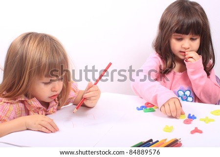 Two little preschool girls, one drawing with pencil the other playing with letters