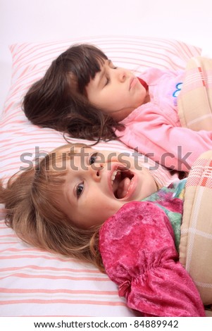 Sleepy little girls just waking up in bed, one still sleeps