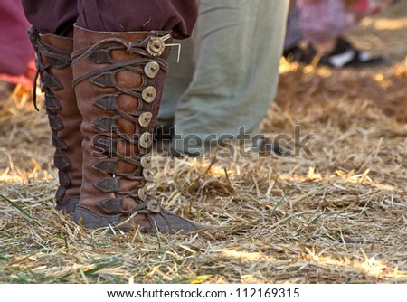 Man standing in grass wearing fancy leather costume boots at a festival.