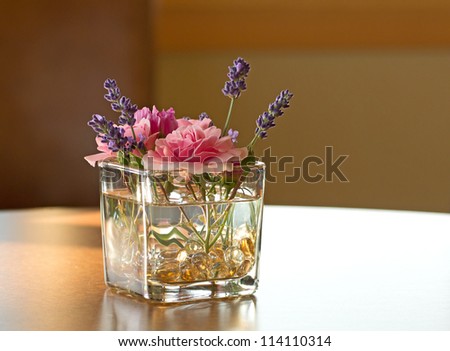 A square glass of colorful flowers in sunlight on a table.