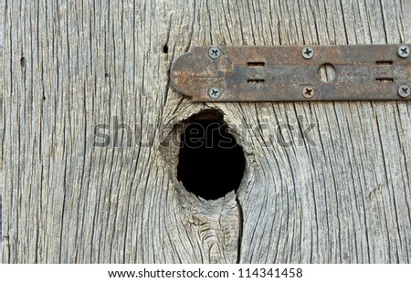 Vintage rusted metal strap on an old board with a big knothole.
