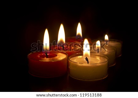 Six red and white tea light candles glowing in the dark