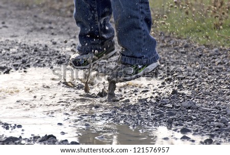 A child\'s feet as he jumps in to a rain puddle