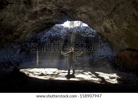 Man with outstretched arms standing in sunbeams shinning down through skylight in cave