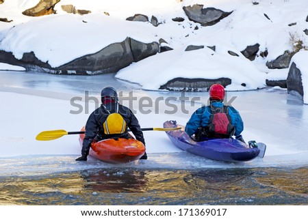 Two men sitting in colorful kayaks resting on an ice flow