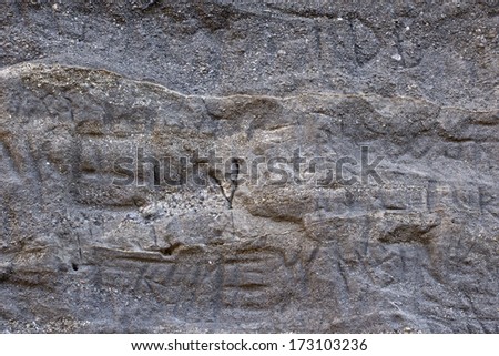 Carved modern graffiti letters on gray rock wall texture