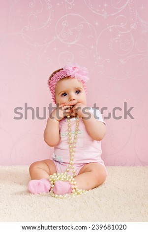 Little girl sitting on the floor holding a pearl necklace