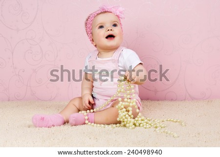 Little girl sitting on the floor holding a pearl necklace on pink background