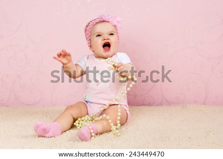 Little girl sitting on the floor holding a pearl necklace on pink background