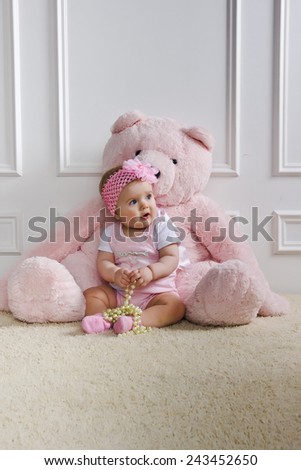 Little girl sitting on the floor holding a pearl necklace with big pink bear
