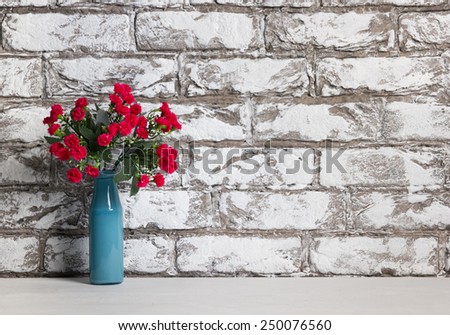 Red flowers in vase on brick wall background