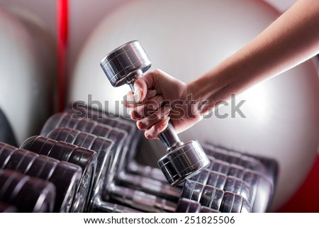 Female hand holding a dumbbell in gym. Sport background.