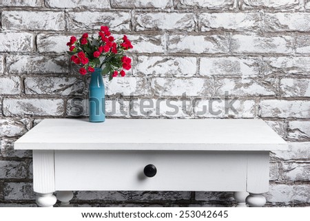 Red flowers in vase on the table on brick wall background
