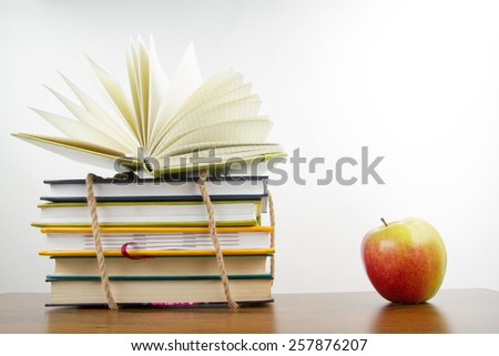 Stack of colorful books tied with a rope, open book and an apple. Back to school on white background. Copy space for text.