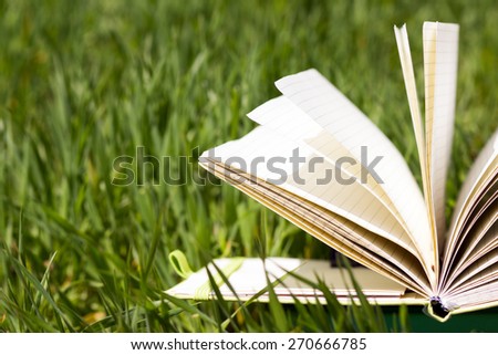 Open book with fanned pages on green grass. Back to school.  Copy Space. Summer spring theme.