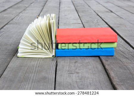 Stack of books and open book with fanned pages on wooden floor and green grass. Back to school. Copy Space. Summer spring theme.