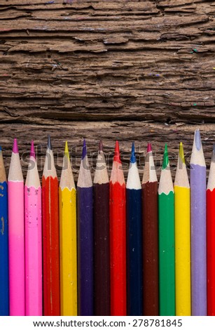 Row of colored drawing pencils closeup on old grunge natural wooden shabby desk background. Vintage stylized image. Copy space