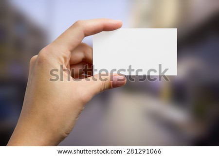 Hand holding a white business visit card, gift, ticket, pass, present close up on blurred blue background. Copy space