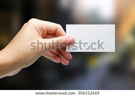 Hands holding a white business visit card, gift, ticket, pass, present close up on blurred blue background. Copy space