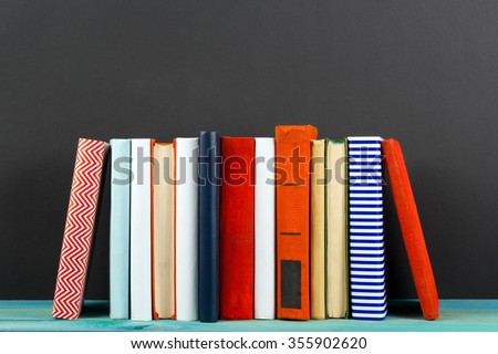 Raw of old vintage colorful hardback books, diary on wooden deck table and black board chalk wall background. Books stacking. Back to school. Copy Space. Education background