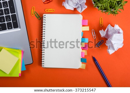 Office table desk with set of colorful supplies, white blank note pad, cup, pen, crumpled paper, flower on red background. Top view and copy space for text