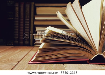 Hardback open old book with fanned pages on wooden grunge shelf table background. Instagram vintage toned photo. Books stacking. Back to school. Copy Space. Education background.