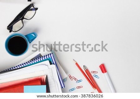 Office table desk with set of colorful supplies, white blank note pad, cup, pen, pc, crumpled paper, flower on white background. Top view and copy space for text