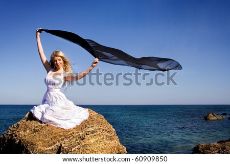 The girl in a white dress holds a scarf on a wind