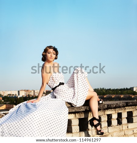 Beautiful young woman with pin-up make-up and hairstyle posing on the roof building.