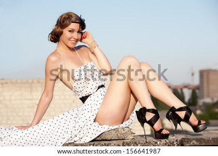 Beautiful young woman with pin-up make-up and hairstyle posing on the roof building.