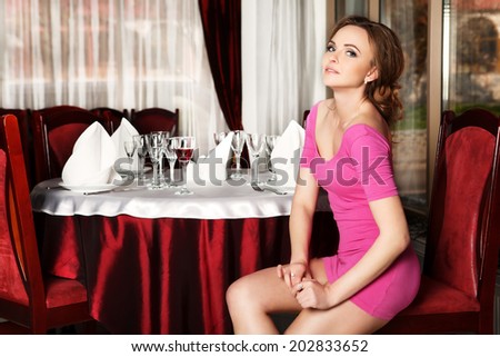 Girl in a short red dress sitting on a chair at a table in the restaurant.